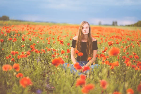 ケシの畑に立つ赤いドレスの美しい女の子 ストック画像