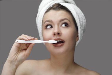 Kafasında havluyla beyaz diş fırçası olan gri bir arka planda Tex için yeri olan bir kız.