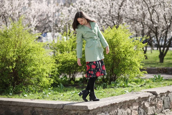 Junge Frau posiert vor grünen Büschen und blühenden Aprikosen — Stockfoto