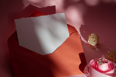 Terracotta zarfının pembe arka planında düğün davetiyeleri için kompozisyon, beyaz bir kağıt, pembe bir kurdele, taşlı bir yüzük. Karşıt gölgeler.