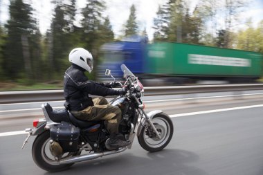 Beyaz kasklı motosikletçi uzun pozlu bir yol çekimi yapıyor.