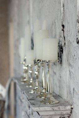 Zarif şamdanlardaki beyaz mumlar odadaki şöminenin üzerinde duruyor.