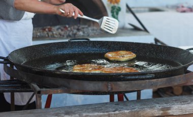 Dişi aşçı, açık havada tereyağlı büyük bir tavada un keki pişiriyor.