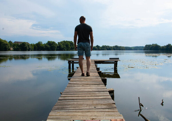 Вид сзади на мальчика в повседневной одежде на деревянном пирсе. летний день. Концепция свободы
