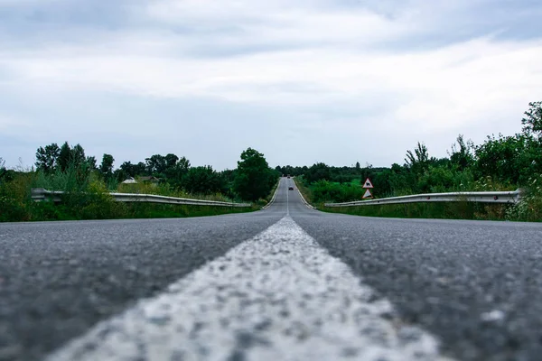 Beyaz yol işaretleri ve kenarlarında yeşil ağaçlar olan boş bir yolda sürüyorlar.