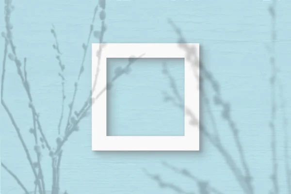 A folha quadrada de papel texturizado branco no fundo da parede azul. Mockup com uma sobreposição de sombras de fábrica. A luz natural lança sombras de ramos de salgueiro. Deitado plano, vista superior — Fotografia de Stock