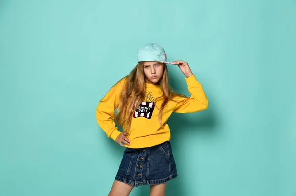 Chica adolescente divertida con gorra de béisbol y sudadera con capucha amarilla posando sobre un fondo azul . —  Fotos de Stock