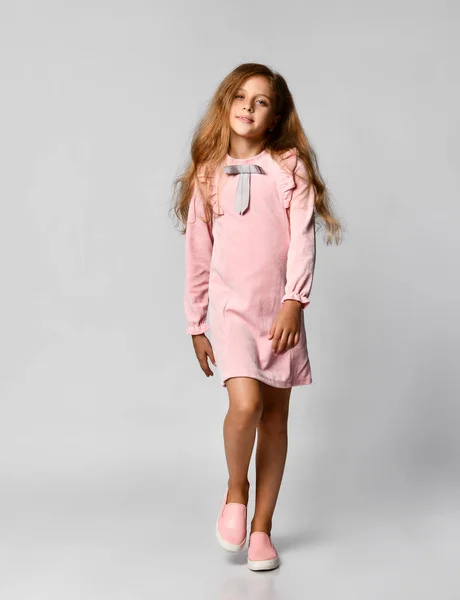 Όμορφο μικρό κορίτσι με μακριά ξανθά μαλλιά και μπλε μάτια, στέκεται σε ένα λευκό φόντο, φορώντας ένα ροζ casual φόρεμα και παπούτσια γυμναστήριο, Έφηβος στυλ — Φωτογραφία Αρχείου