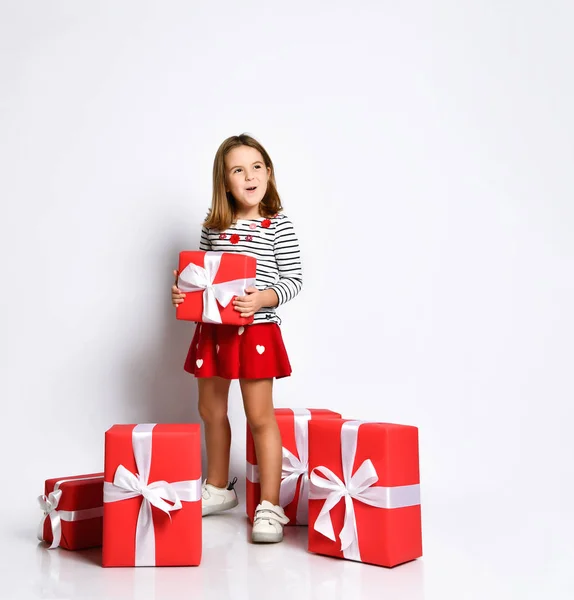 Happy cute young girl holding a red gift box with a white ribbon over a light background — Stock Photo, Image