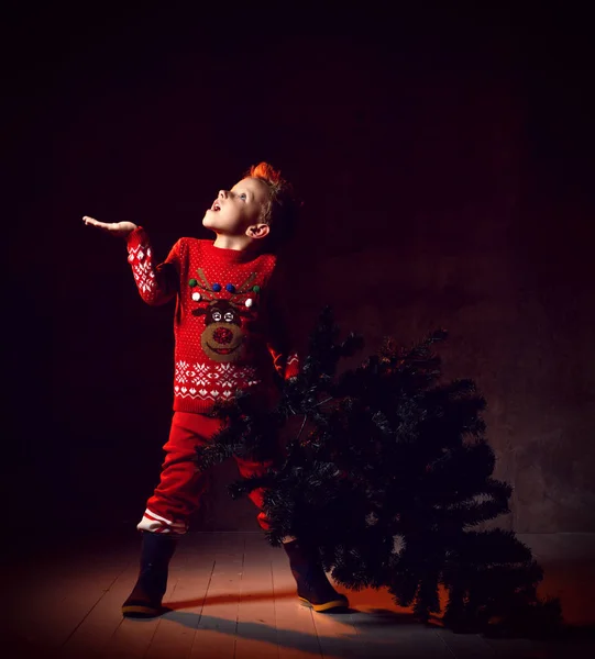 Маленький мальчик держит рождественскую елку в одной руке, а второй пытается поймать снежинки — стоковое фото