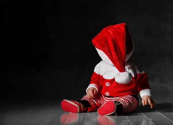 빨간 스웨터를 입고 산타 모자를 쓰고 어두운 배경에 앉아 있는. — 스톡 사진