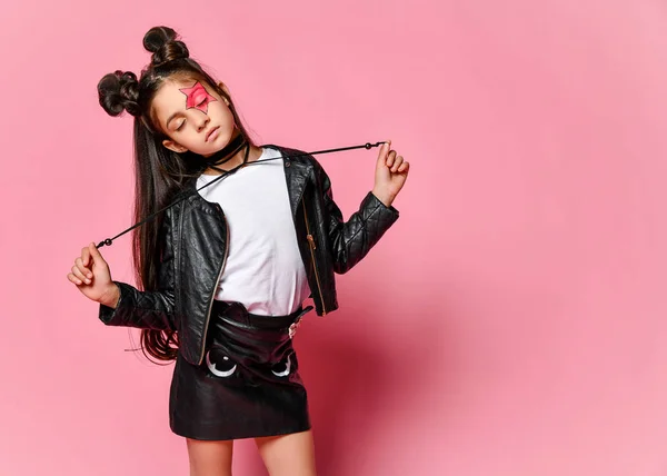 Menina hipster em uma jaqueta de couro preto posando em um fundo rosa, segurando os laços do colar . — Fotografia de Stock