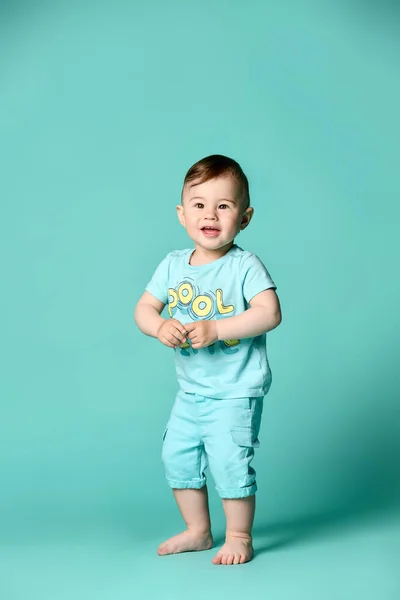 Full längd porträtt av ett småbarn pojke i en blå sommar bomull kostym isolerad i en turkos bakgrund. — Stockfoto