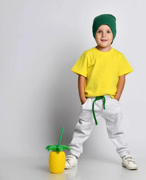 El niño bebe una bebida de cóctel en forma de piña con una pajita de cóctel. Vestido con una camiseta amarilla sobre un fondo blanco —  Fotos de Stock