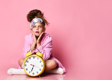 Yerde sabahlıkla otururken elinde çalar saat tutan esneyen genç kız..