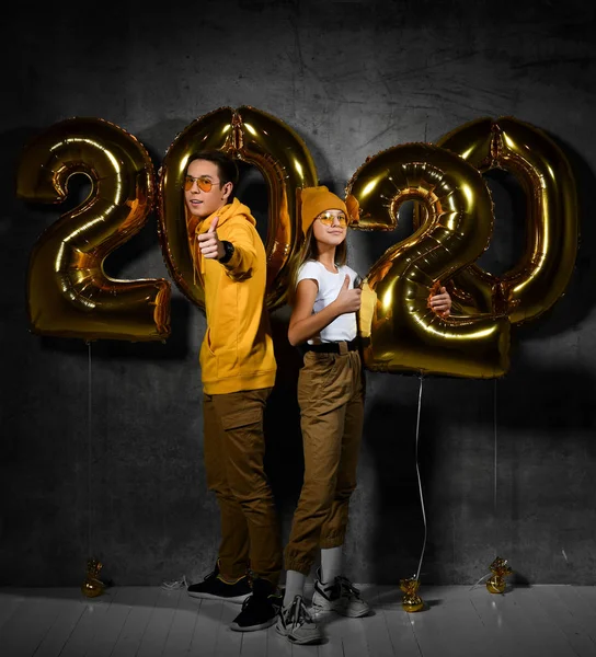 Dos amigos felices chico y una chica están celebrando una fiesta de año nuevo con números de ballonss 2020 sobre un fondo concreto . — Foto de Stock