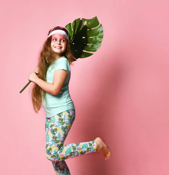 Grappig kind meisje loopt en springt met een grote tropische palm blad op een gekleurde achtergrond — Stockfoto