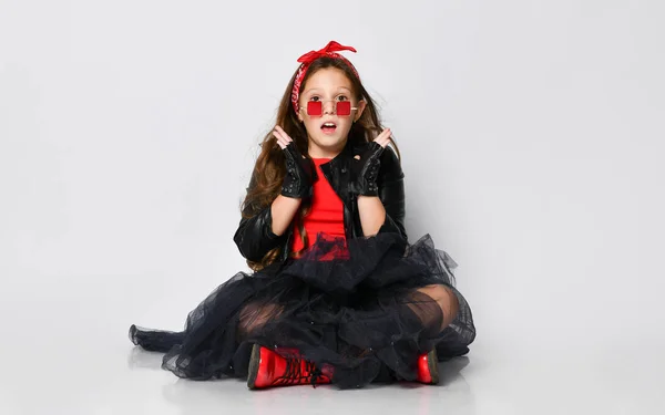 Jong positief meisje model in heldere rock stijl casual kleding en rode laarzen zitten op de vloer en het gevoel verrast — Stockfoto
