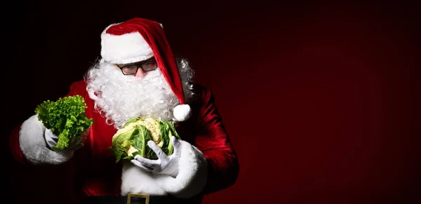 Jolly Santa Claus holds in one hand a bunch of lettuce in another swing of cauliflower. The choice. Enjoy a healthy Christmas dinner. Healthy Christmas Recipes. — Stock Image Jolly Santa Claus holds in one hand a bunch of lettuce in another swing of cauliflower. The choice. Enjoy a healthy Christmas dinner. Healthy Christmas Recipes. Royalty Free Stock Photos