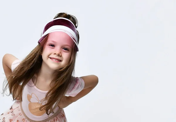 Klein lachend schattig meisje in casual zomer jurk, hoed en sneakers staan en poseren over witte muur achtergrond — Stockfoto