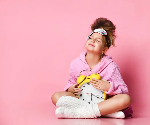 Geeuwen tiener meisje met een wekker terwijl zitten in een huisjas op de vloer. — Stockfoto