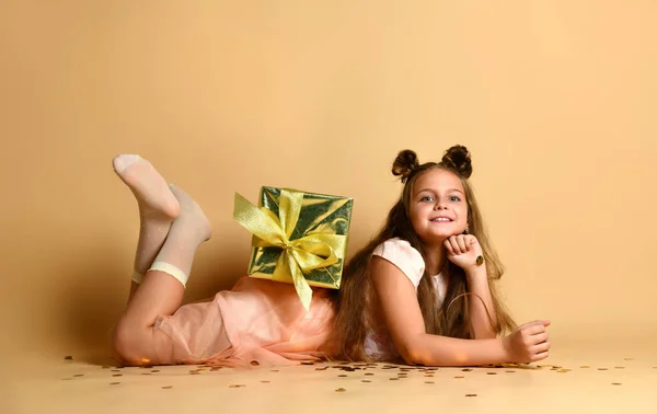 Mooi klein meisje liggend op de vloer met een geschenkdoos in de studio — Stockfoto