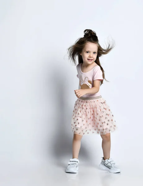 Klein lachend schattig meisje in casual zomer jurk en sneakers lopen in actie over witte muur achtergrond — Stockfoto