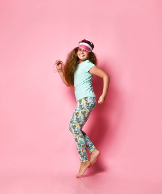 Stüdyoda pembe arka planda şapkalı bir kız kameraya bakıyor.