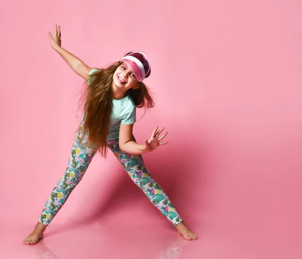 Uma menina em um boné no estúdio em um fundo rosa caretas olhando para a câmera — Fotografia de Stock