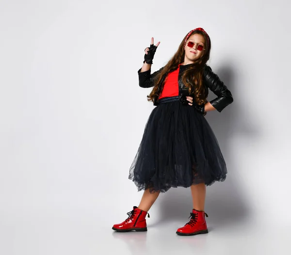 Joven chica positiva más tamaño en ropa de estilo rock, botas rojas y gafas cuadradas de pie y mostrando signo de paz con los dedos — Foto de Stock