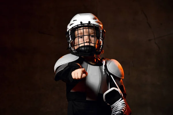 Chłopiec w mundurze hokejowym i kasku ochronnym z łyżwami hokejowymi stojącymi i wskazującymi kamerą palcem — Zdjęcie stockowe