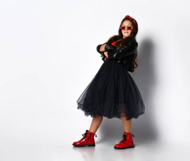 Genç, pozitif, taş gibi giyinen, kırmızı çizmeli ve kare gözlüklü beyaz arka planda poz veren kız model.