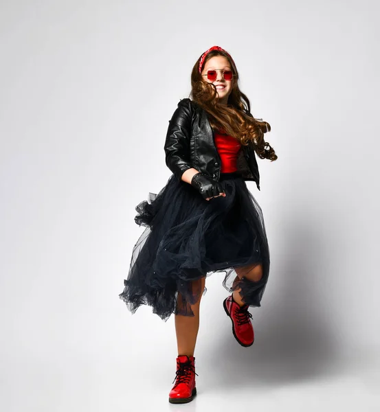 Joven modelo de chica positiva de talla grande en ropa de estilo rock brillante, botas rojas y gafas cuadradas bailando sobre fondo blanco — Foto de Stock