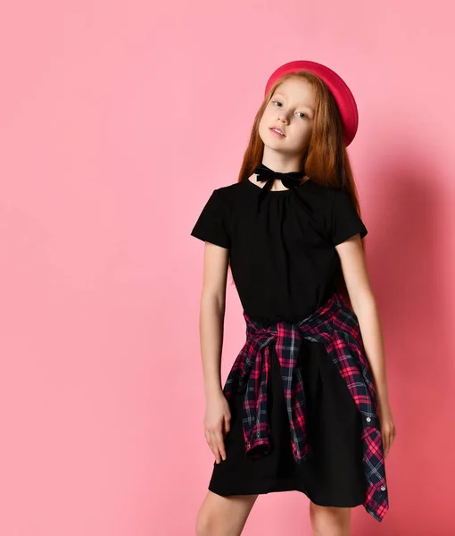 Ginger tienermeisje in zwarte jurk, geruite shirt op middel, rode hoed en choker. Ze glimlacht, poseert op een roze achtergrond. Sluiten. — Stockfoto