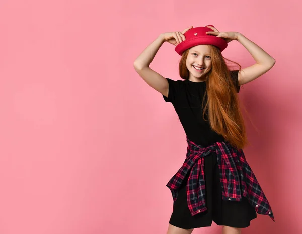Tiener in zwarte jurk, geruit shirt aan de taille. Ze glimlachte, raakte haar rode hoed aan, poseerde op een roze achtergrond. Sluiten. — Stockfoto