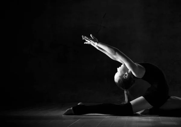 Ung flicka gymnast i svart sport kropp och speciella skor gör gymnastik pose över mörk bakgrund — Stockfoto