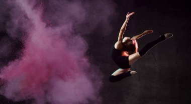 Siyah spor vücutlu genç bir jimnastikçi ve renkli ışıltılarla karanlık arka planda daireler çiziyor.