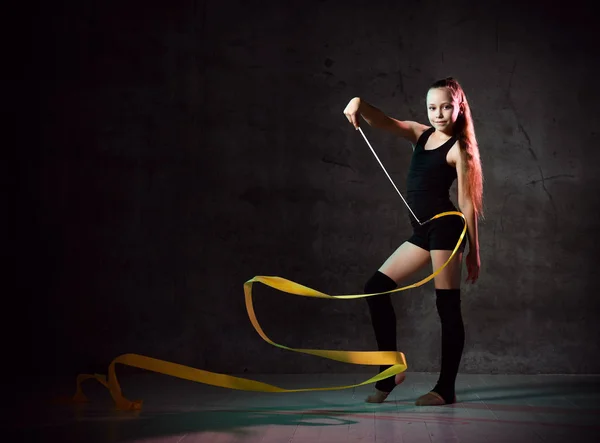 Portret pięknej młodej brunetki gimnastyczka trening gimnastyczny ćwiczenia z żółtą wstążką na tle ciemnego dymu studio. — Zdjęcie stockowe