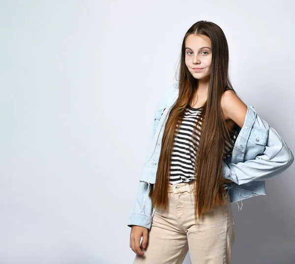 Tienermeisje in gestreept t-shirt, spijkerjasje en broek. Ze kijkt naar je, poseert geïsoleerd op een witte studio achtergrond. Sluiten. — Stockfoto