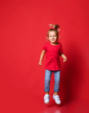 Küçük, mutlu, heyecanlı, şık giyimli ve kırmızı duvardan atlayan beyaz spor ayakkabılı sarışın kız.