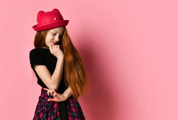 Fekete ruhás tinédzser, kockás ing a derekán, piros kalap. Gondolta, megérinti az arcát, rózsaszín háttérrel pózol. Közelről. — Stock Fotó