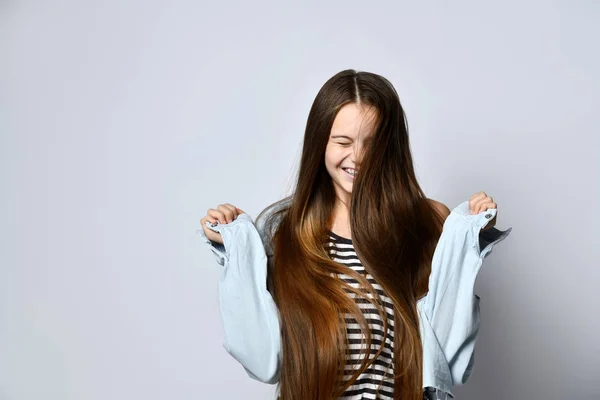 Adolescente de pelo largo, con camiseta a rayas y chaqueta vaquera. Ella se ríe, posando aislada en el fondo del estudio blanco. —  Fotos de Stock