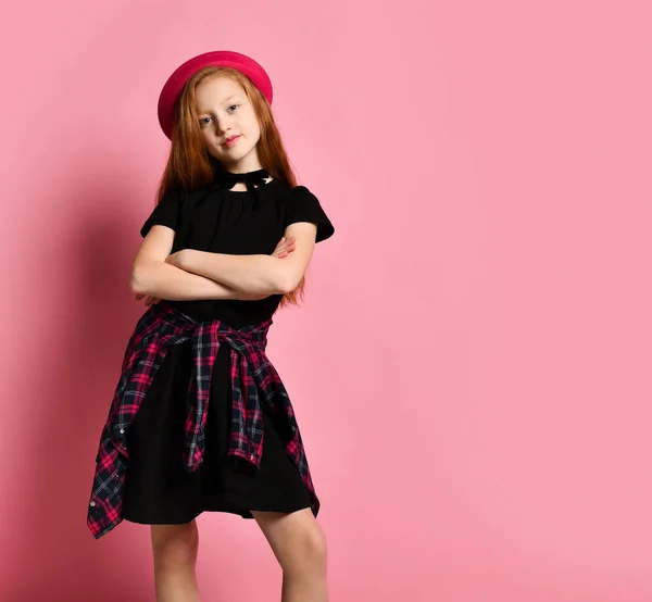 Ginger teenage kid in black dress, checkered shirt, red hat and choker. Smiling, hands foled, posing on pink background. Close up — ストック写真