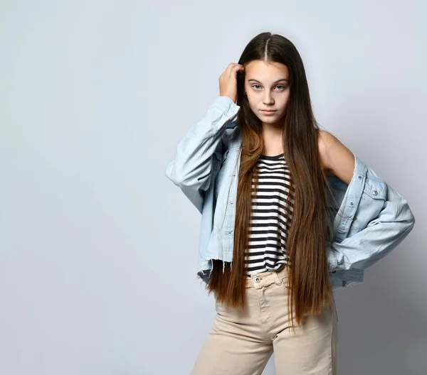 Tienermeisje in gestreept t-shirt, spijkerjasje en broek. Ze kijkt naar je, poseert geïsoleerd op een witte studio achtergrond. Sluiten. — Stockfoto