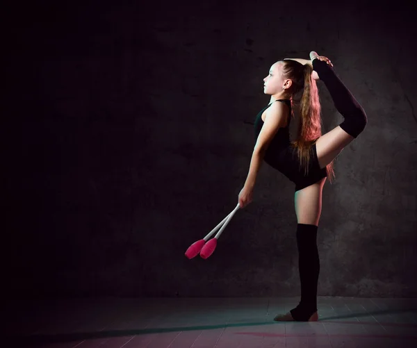 Молода усміхнена дівчина-гімнастка в чорному спортивному тілі і підйомники стоять і тримають дві рожеві гімнастичні маски в руці — стокове фото