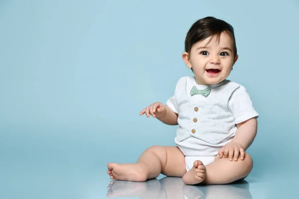 Маленька дитина в білому костюмі як жилет з носовою краваткою, босоніж. Він посміхається, сидячи на підлозі на синьому фоні. крупним планом — стокове фото