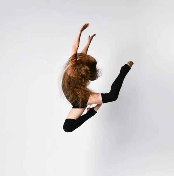 Молодая девушка гимнастка в черном спортивном теле и верхние прыжки и принятия династической позы в воздухе на белом фоне — стоковое фото