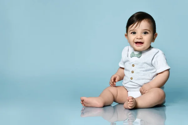 弓タイ、裸足でベストとして白いボディスーツの赤ちゃんの男の子。彼は笑顔で、青い背景を背景に床に座っている。閉じろ! — ストック写真