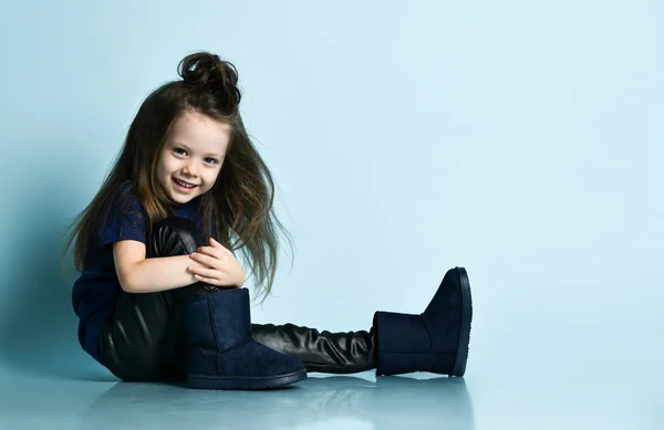 Klein lachend meisje model met lang haar in stijlvolle casual kleding en ugg laarzen zitten op de vloer — Stockfoto