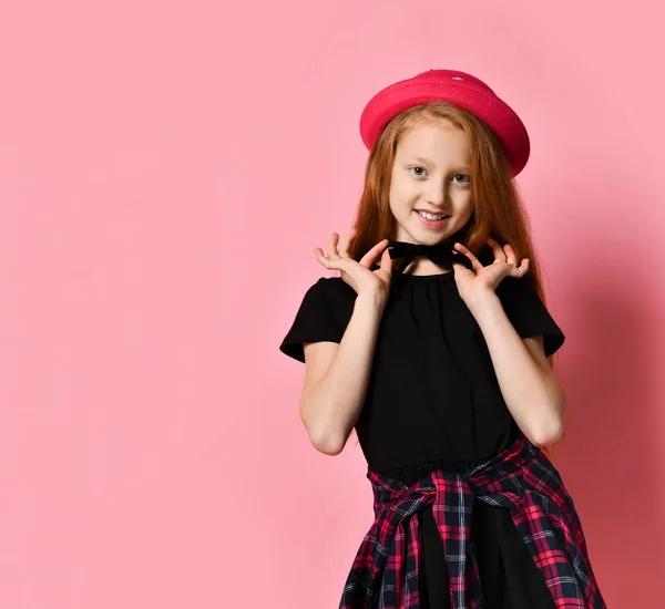 Tiener kind in zwarte jurk, geruite shirt op de taille, rode hoed. Glimlachen, haar wurggreep vasthouden, poseren op een roze achtergrond. Sluiten. — Stockfoto